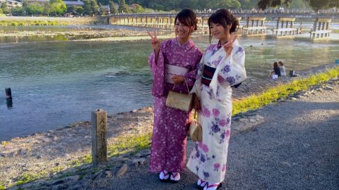 Kimono-clad Japanese tourists pose in front of Arashiyama's Togetsukyo Bridge. 