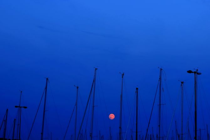 The moon is seen among the masts of sailing boats in Fiskeback Harbor, outside of Gothenburg, Sweden.