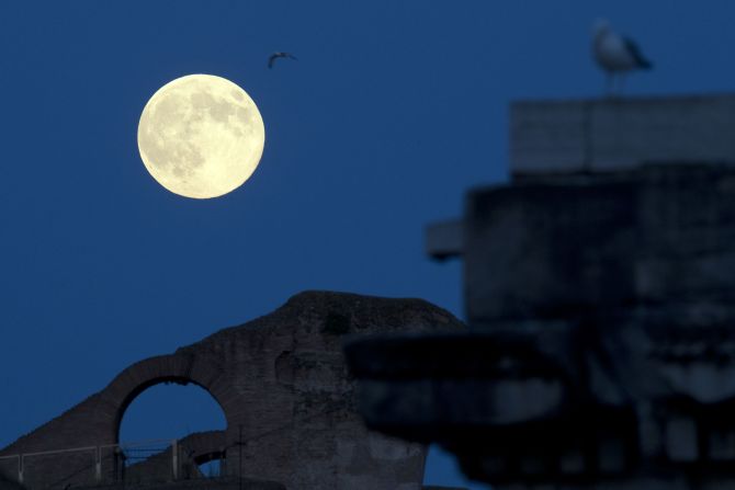 The moon appears above the Colosseum in Rome.