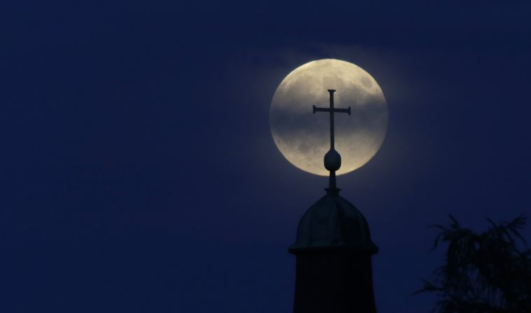 The moon appears behind a cross of the Christkoenig Church in Munich, Germany.