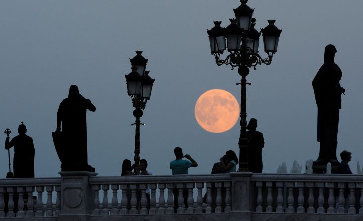 People take photos as the moon rises above a bridge over Vardar River in Skopje, Macedonia.