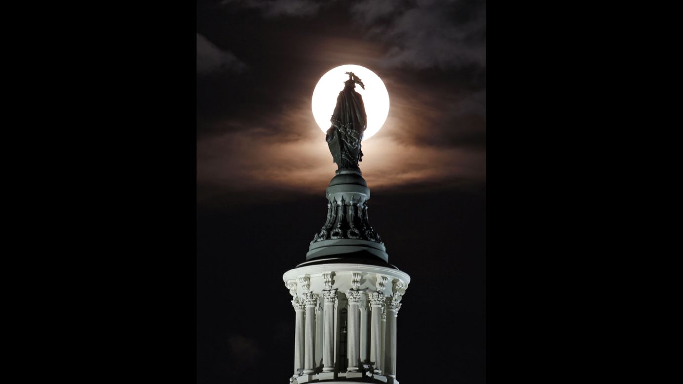 The moon rises through clouds behind the bronze Statue of Freedom by Thomas Crawford atop the U.S. Capitol in Washington. 