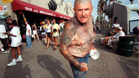 A tatooed man walks by Muscle Beach, an open-air weight-lifting facility (R), in Venice Beach, CA, 13 August. Venice Beach is touted southern California's second major attraction after Disneyland. This popular playground draws 300,000 to 350,000 visitors on weekends from late spring into early fall as well as hundreds of thousands on weekdays and off season, according to figures provided by the Venice Boardwalk Association.