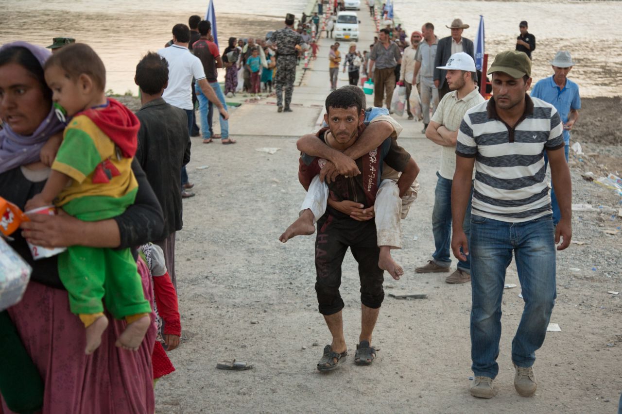 A young refugee carries a disabled man across the bridge.