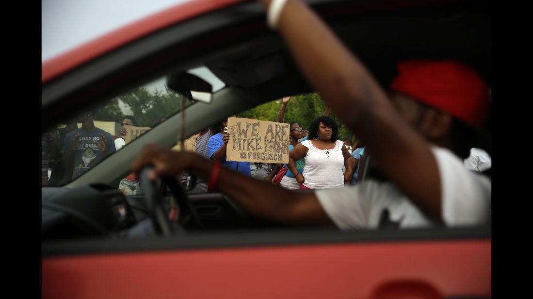 Demonstrators hold signs as traffic moves slowly past them on August 14, 2014.