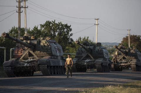 A Ukrainian soldier walks past a line of self-propelled guns as a column of military vehicles prepares to head to the front line near Ilovaisk on Thursday, August 14.