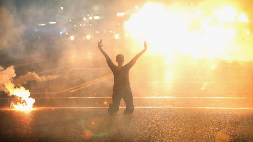Tear gas reigns down on a woman kneeling in the street with her hands in the air after a demonstration over the killing of teenager Michael Brown by a Ferguson police officer on August 17, 2014 in Ferguson, Missouri. Despite the Brown family's continued call for peaceful demonstrations, violent protests have erupted nearly every night in Ferguson since his August 9, death. 