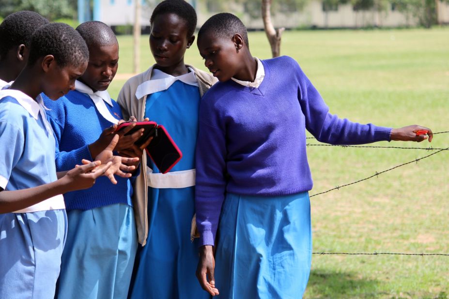 A group of female students gather around an e-reader in Amogoro. The devices can hold a charge for up to two weeks, which is helpful in areas where electricity is scarce.
