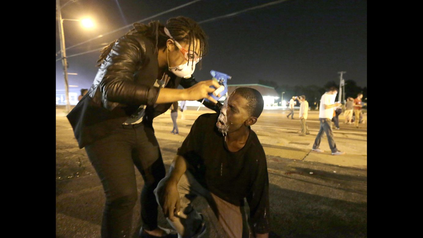A woman helps a man affected by tear gas August 18, 2014. The situation overnight deteriorated after a handful of protesters threw rocks, bottles and Molotov cocktails at police. Officers responded by firing stun grenades and tear gas canisters.