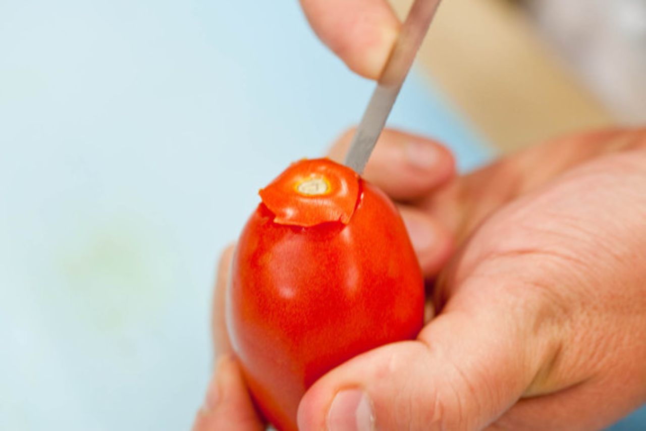 Start by coring 4 pounds of tomatoes using a paring knife to cut a cone shape out of the top of each one.