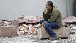 Ron Peralez, of Vacaville, Calif., sits on rubble and looks at earthquake-damaged buildings Monday, Aug. 25, 2014, in Napa, Calif. The San Francisco Bay Area's strongest earthquake in 25 years struck the heart of California's wine country early Sunday, igniting gas-fed fires, damaging some of the region's famed wineries and historic buildings, and sending dozens of people to hospitals. (AP Photo/Eric Risberg)