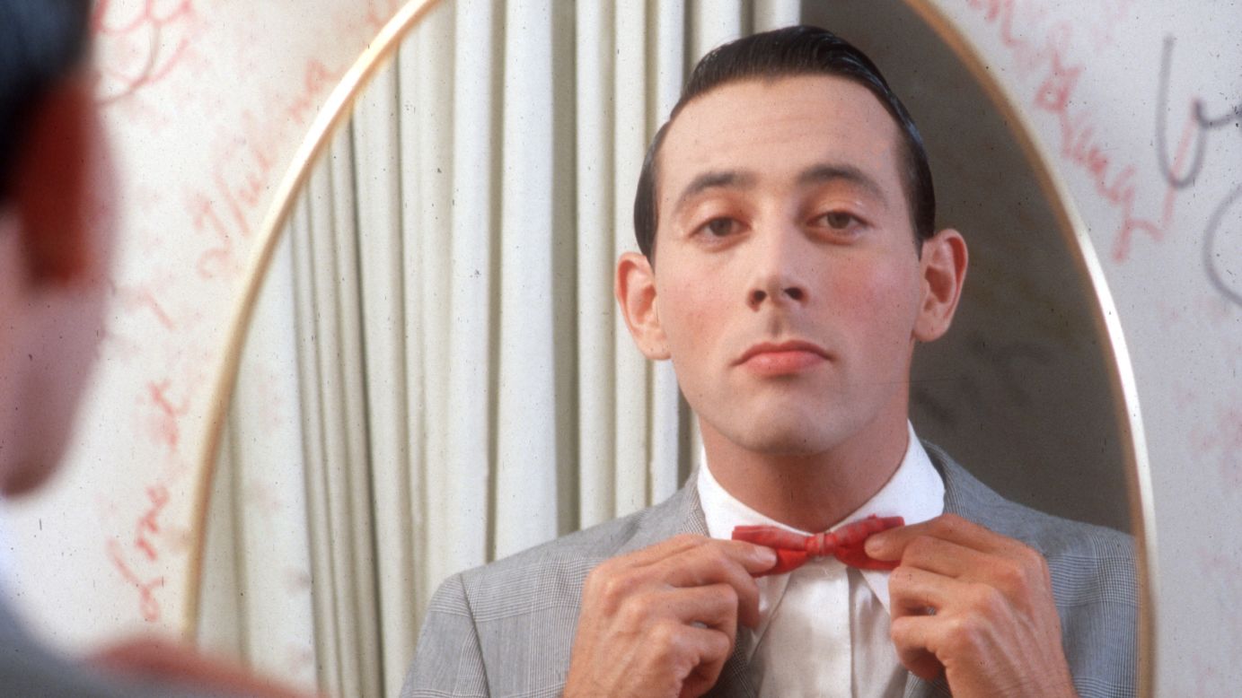 Beloved performer Pee-wee Herman, here circa 1980, straightens his characteristic red bow tie, which he always pairs with a light gray suit.