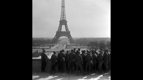 German soldiers on the Esplanade du Trocadero view the Eiffel Tower. In June 1940, German troops marched into Paris, forcing France to capitulate and establish the pro-Axis Vichy French government.