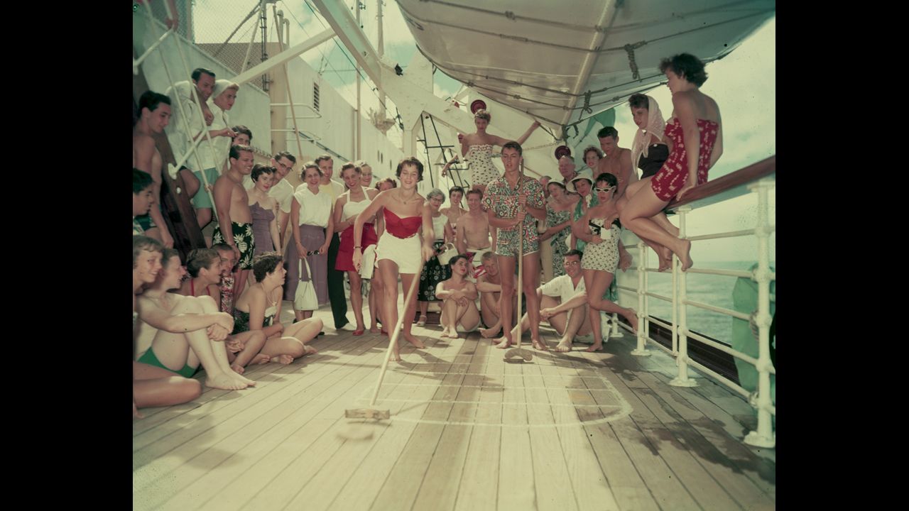 Watched by a crowd of fellow cruise passengers, Judy Topping uses a cue to "shoot" a disc along a shuffleboard court during a cruise on the SS Lurline in 1954. 