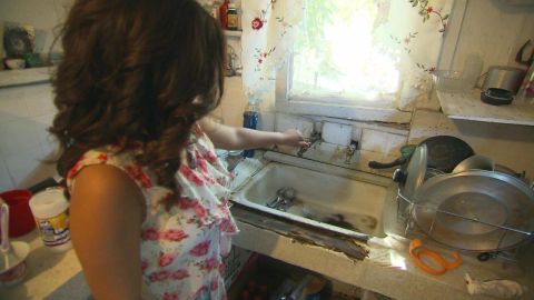 Sandra Tapia uses a hose hookup to a neighbor's house to wash dishes.