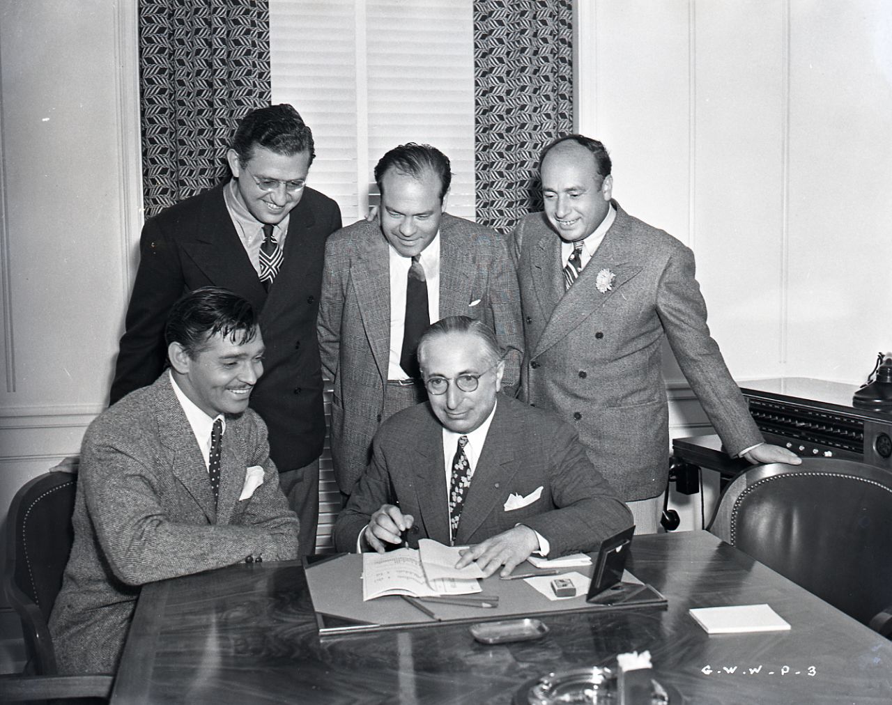 For publicity purposes, Clark Gable, the overwhelming popular choice to play Rhett Butler, pretends to sign a contract for the film under the watchful eye of producer Selznick, standing, far left, and MGM studio chief Louis B. Mayer, seated right. The star had been reluctant to tackle the role, fearing he wouldn't be able to live up to the public's expectations. With Gable now available, Selznick had to move quickly to start filming. 