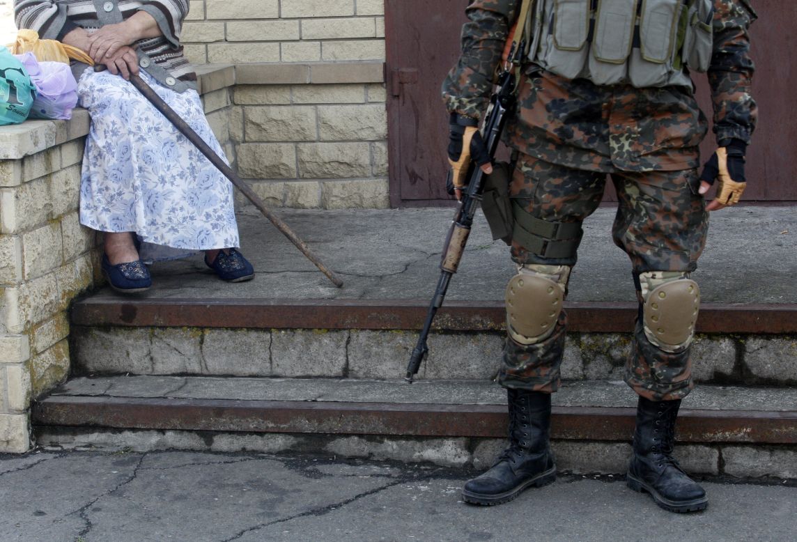 An elderly woman sits next to a Ukrainian soldier standing guard in Volnovakha on September 11.