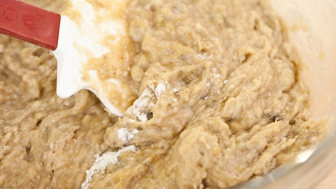 8. Pour banana mixture into dry ingredients. Stir until just combined; some streaks of flour will remain. Fold in walnuts, if using. Scrape batter into prepared pan.