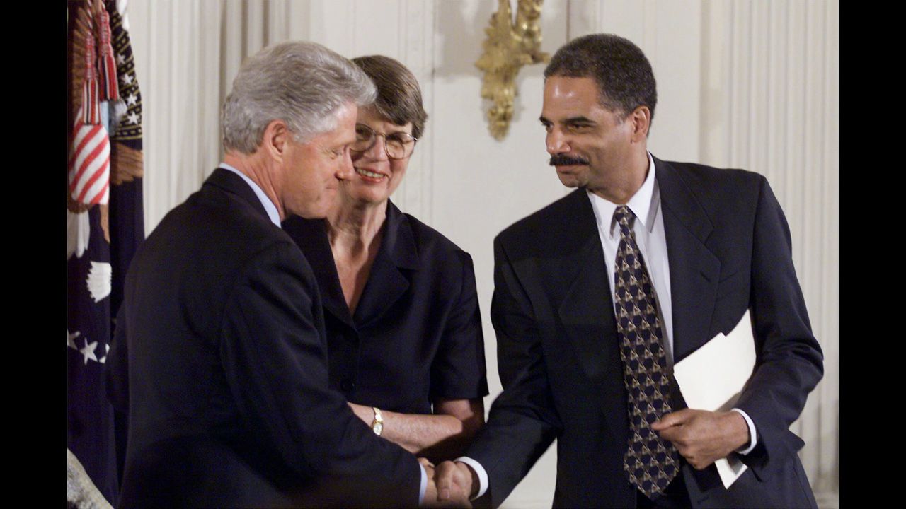 Holder shakes hands with then-President Bill Clinton as Attorney General Janet Reno, Holder's boss, looks on at an American Bar Association event at the White House in 1999.
