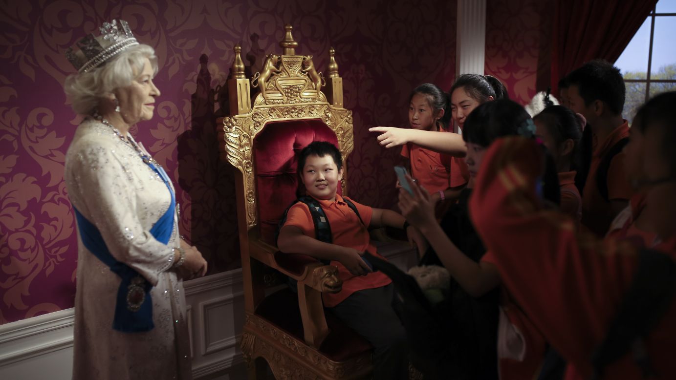 A student, sitting on a mock-up of a royal throne, looks at a wax figure of Britain's Queen Elizabeth II while other students take photos Friday, September 19, at the Madame Tussauds museum in Beijing.
