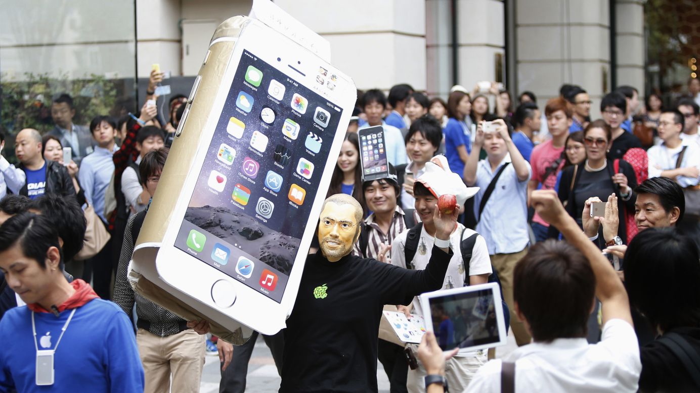 A man wearing a mask of Apple co-founder Steve Jobs holds a cardboard cutout of Apple's new iPhone 6 as he walks into an Apple Store in Tokyo on Friday, September 19.