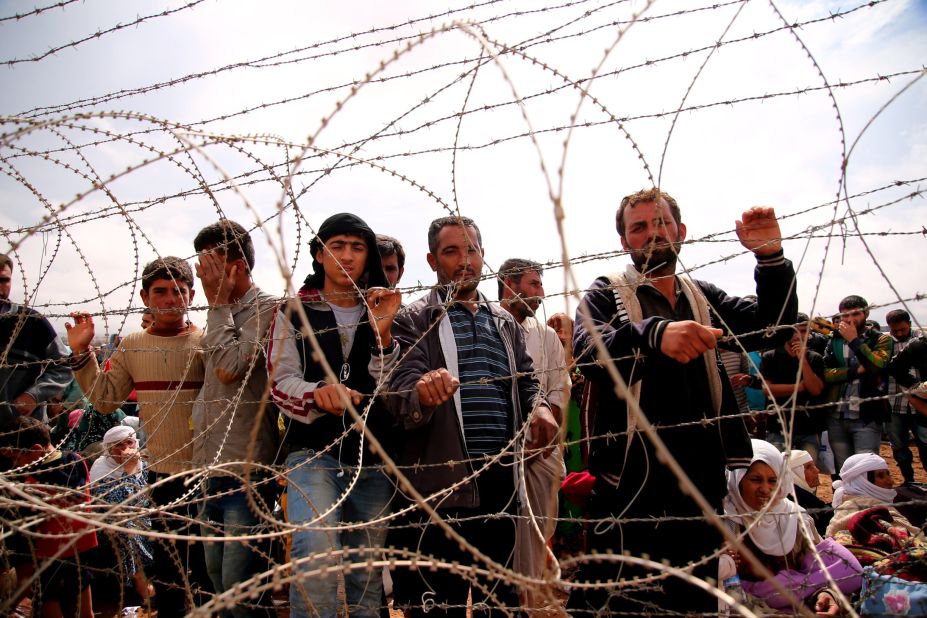 Syrian Kurds wait behind border fences to cross into Suruc on Sunday, September 28.