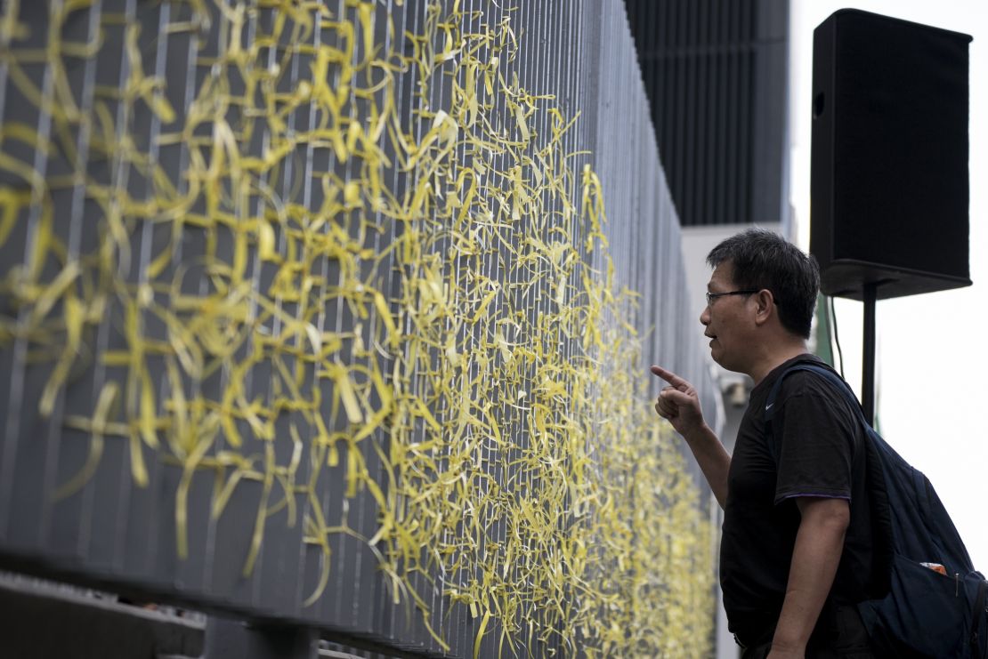 A pro-democracy activists shouts at police officers behind a fence with yellow ribbons tied to it by protesters at the entrance to the government headquarters in Hong Kong.