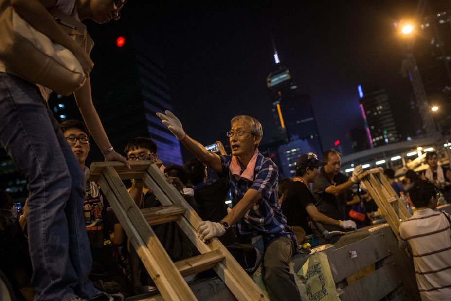 A man helps protesters use a makeshift ladder to climb over concrete street barricades on September 29.