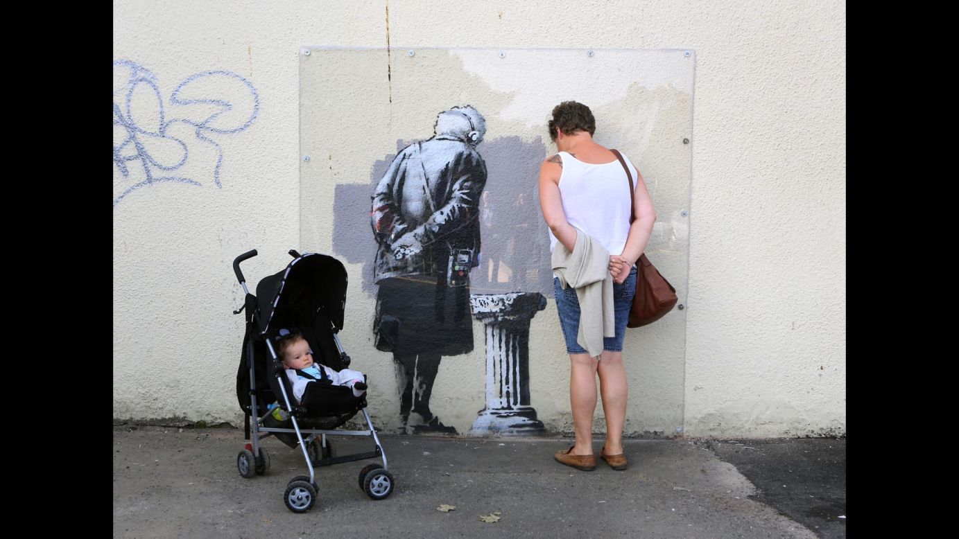 A woman poses next to a mural, created by street artist Banksy, in Folkestone, England, on Tuesday, September 30.