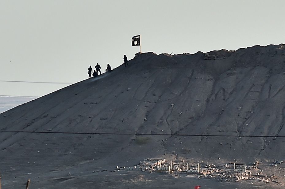 Alleged ISIS militants stand next to an ISIS flag atop a hill in Kobani on Monday, October 6.