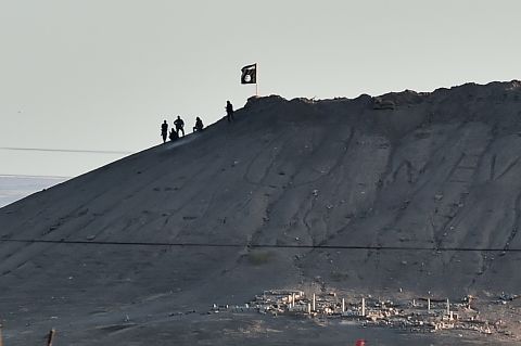 Alleged ISIS militants stand next to an ISIS flag atop a hill in Kobani on Monday, October 6. 
