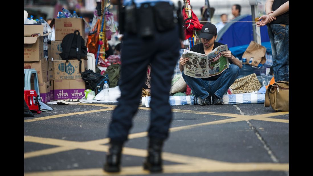 A pro-democracy protester reads a newspaper in Hong Kong's Mong Kok district on Tuesday, October 7, as a police officer stands nearby.