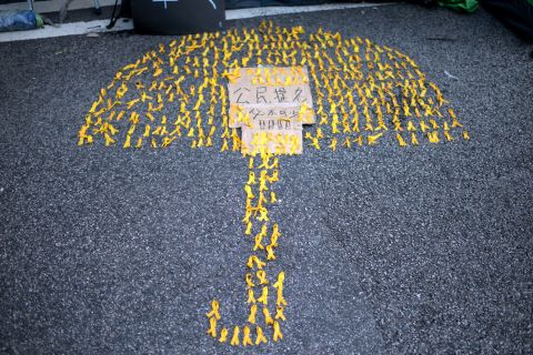 An image of an umbrella made up of yellow ribbons is laid out on the ground near the central government offices. The sign reads: "We can't live without civic nominations."