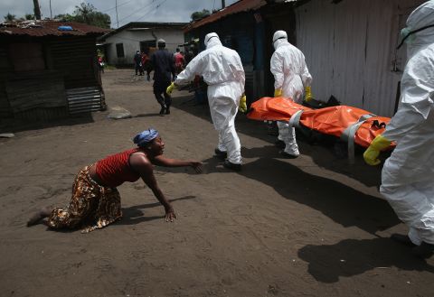 A woman crawls toward the body of her sister as a burial team takes her away for cremation October 10, 2014, in Monrovia. The sister had died from Ebola earlier in the morning while trying to walk to a treatment center, according to her relatives.