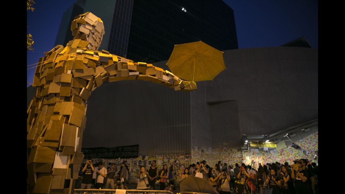 People gather beneath the statue "Umbrella Man," by the Hong Kong artist known as Milk, which has become a symbol at the protest site, on Saturday, October 11, in Hong Kong.