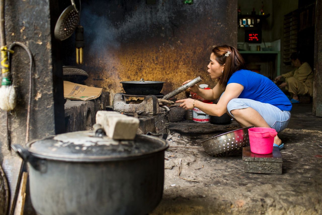 A woman at the restaurant blows on the coals to keep the flames going for a meal.