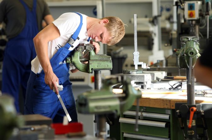The country's unique apprenticeship scheme has played a key role in nurturing Germany's manufacturing success, with school leavers spending around 2-3 years training with companies. A trainee, pictured, files a piece of metal at a Siemens training center in Berlin.