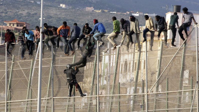 A policeman with the Spanish Civil Guard pulls a sub-Saharan migrant Wednesday, October 15, as he climbs up a border fence dividing Morocco and the Spanish enclave of Melilla. About 200 migrants tried to reach Melilla in what was the second mass attempt in a 24-hour period.