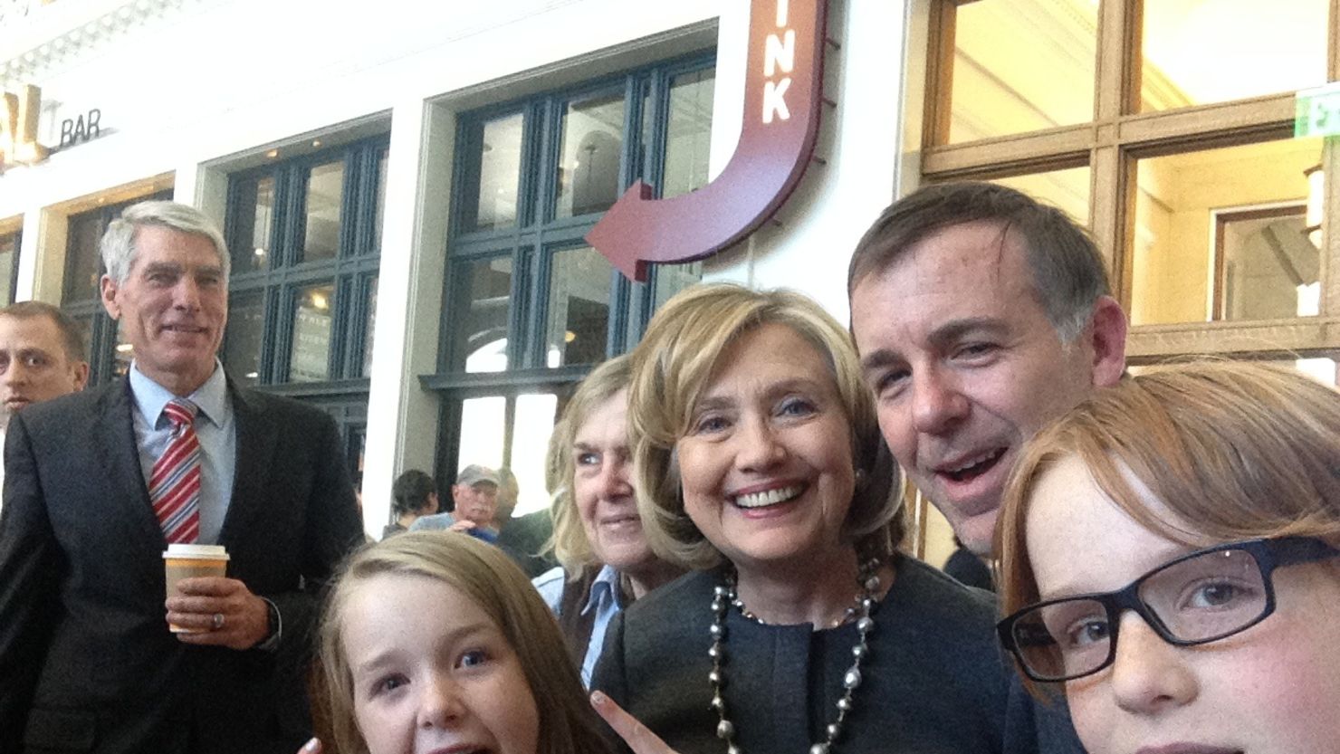 Macy Friday, flashing peace signs, poses with (right to left) her 12-year old brother Finn, her father Derek, Hillary Clinton and her grandmother Elaine. Sen. Mark Udall photobombs on the left.