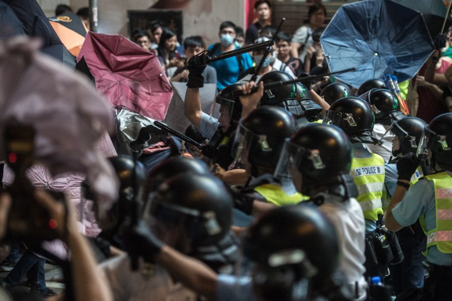 Police use batons to hit pro-democracy protesters who are using raised umbrellas for protection on October 17. 