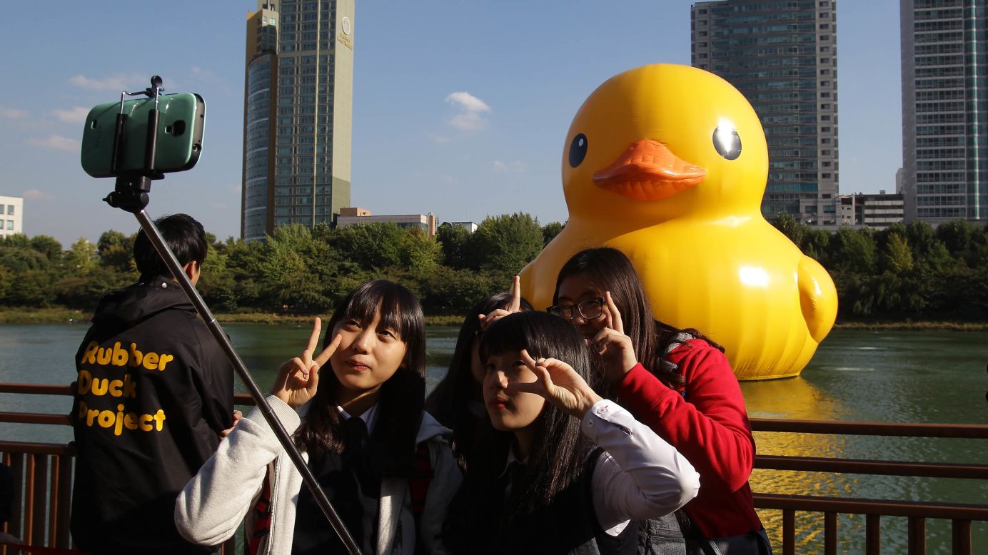 People show peace signs in front of a giant rubber duck floating in Seoul, South Korea, on Wednesday, October 15. The large duck, created by Dutch artist Florentijn Hofman, will be on display in Seoul until November 14.
