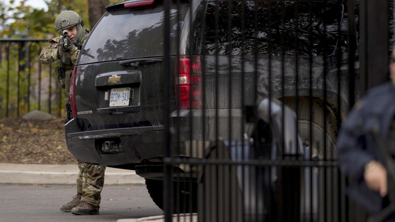 A heavily armed officer takes position at the gate of 24 Sussex Drive, the official residence of Canadian Prime Minister Stephen Harper. Harper was evacuated from the Parliament building, his press secretary tweeted.