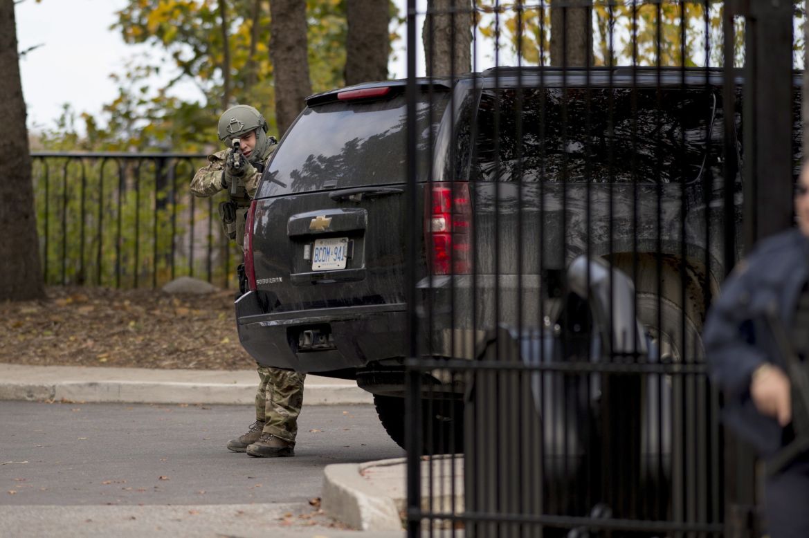 A heavily armed officer takes position at the gate of 24 Sussex Drive, the official residence of Canadian Prime Minister Stephen Harper. Harper was evacuated from the Parliament building and is safe, his press secretary tweeted.