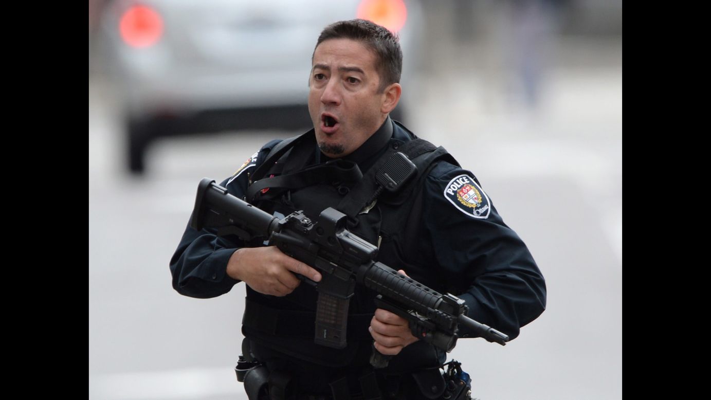 A police officer runs with his weapon drawn outside Parliament Hill.