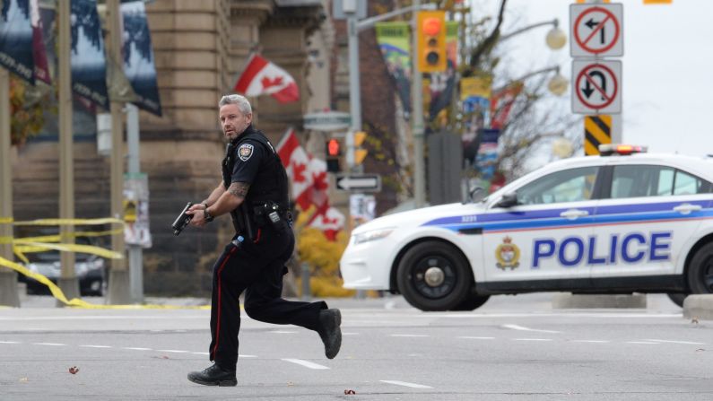 A police officer runs with his weapon drawn outside Parliament Hill.