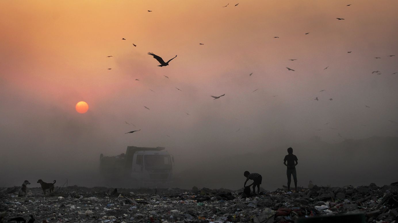 A thick blanket of smoke is seen against the setting sun as young people look for reusable material at a garbage dump in New Delhi on Friday, October 17.