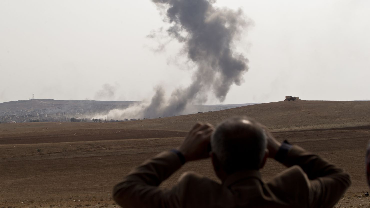 A man watches through binoculars as smoke rises over Kobani during airstrikes by the US-led coalition on October 28, 2014.