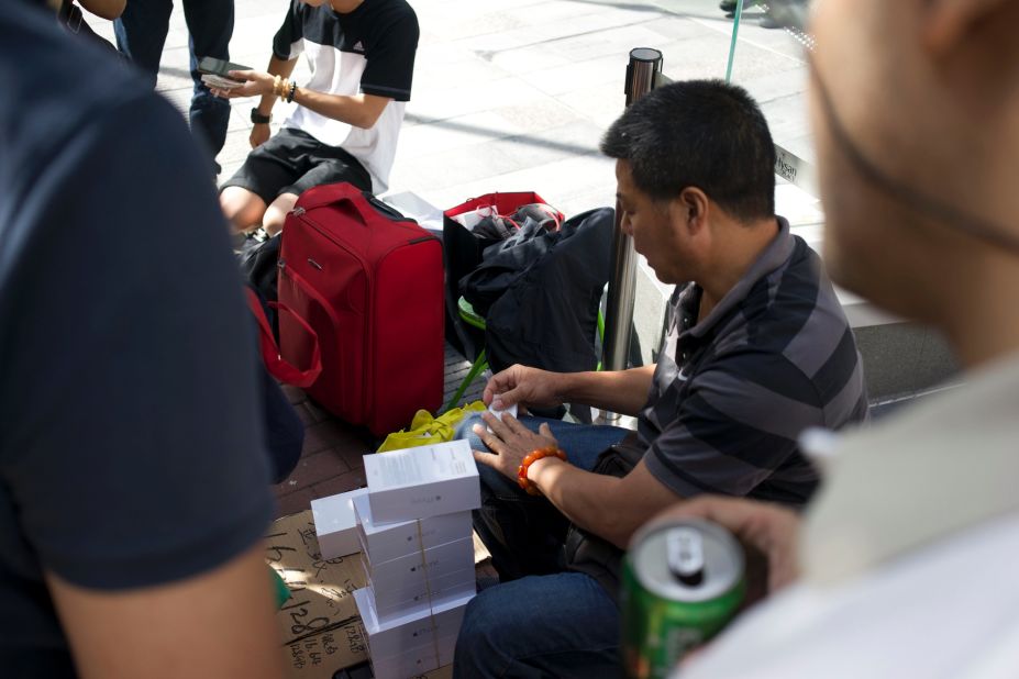 Resellers sit on cheap plastic chairs with their open suitcases beside them, stacked up with white boxes. 