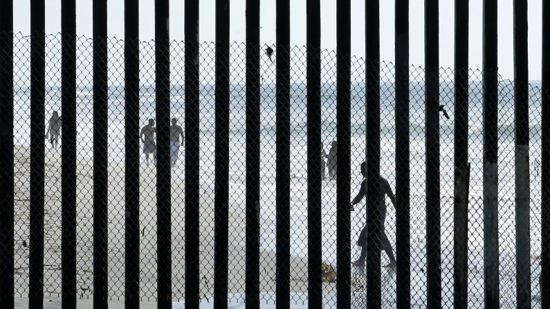 People walk along a beach in Tijuana, Mexico, on Wednesday, October 29. The metal bars in the foreground mark Tijuana's border with the United States.