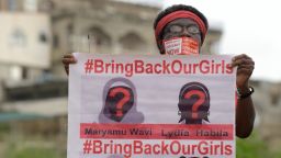 Caption:A supporter of the #BringBackOurGirls campaign carries a placard showing the missing faces of the kidnapped Chibok schoolgirl during a demonstration in the Nigerian capital Abuja on October 14, 2014. Nigerian police on Tuesday blocked supporters of 219 schoolgirls kidnapped by Boko Haram militants from marching on the president's official residence on the six-month anniversary of the abduction. A wall of female officers in full riot gear formed the first line of a barricade in front of less than 100 members of the Bring Back Our Girls campaign, preventing them from setting out.AFP PHOTO/PIUS UTOMI EKPEI (Photo credit should read PIUS UTOMI EKPEI/AFP/Getty Images)